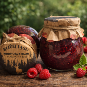 Dwa słoiki konfitury malinowej Bliżej Lasu na drewnianym stole, udekorowane papierem kraft i jutowym sznurkiem, w otoczeniu świeżych malin i zielonych liści.