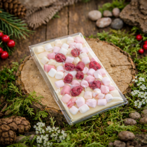 Biała czekolada z piankami marshmallow i malinami w leśnej aranżacji na drewnianym krążku