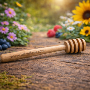 Drewniany nabierak do miodu z grawerem www.blizejlasu.com leżący na rustykalnym stole w ogrodowym, kwiatowym tle.