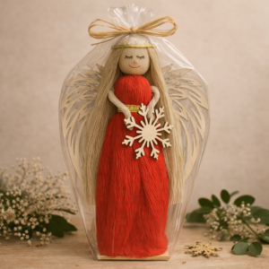 Ręcznie wykonana figurka czerwonego anioła z drewnianymi skrzydłami i ozdobą w kształcie płatka śniegu, zapakowana w przezroczystą folię.
