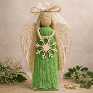 Ręcznie wykonana figurka zielonego anioła z drewnianymi skrzydłami i ozdobą w kształcie płatka śniegu, zapakowana w przezroczystą folię.