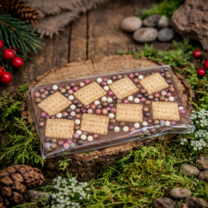 Czekolada mleczna z ciasteczkami i kolorowymi drażetkami w leśnej aranżacji na drewnianym krążku