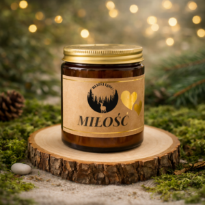 Świeca sojowa „MIŁOŚĆ” w bursztynowym słoiku ze złotą pokrywką na drewnianej podstawie, w eleganckiej leśnej aranżacji z delikatnym światłem bokeh.