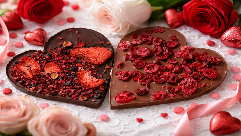 Czekoladowe serca z liofilizowanymi malinami i truskawkami, ułożone na eleganckim tle z różami i dekoracjami walentynkowymi.